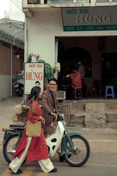 a man and woman riding on the back of a scooter down a street