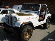 an old white jeep parked in front of a brick building next to a police car