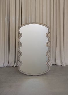 a large round mirror sitting on top of a floor next to a curtained window