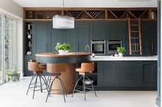 a kitchen with dark green cabinets and wooden stools, white flooring and an island in the middle