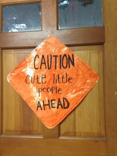 an orange caution sign that says caution cute little people ahead on the side of a door