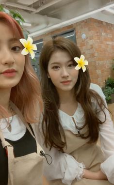 two young women with flowers in their hair posing for the camera while wearing aprons