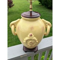 a large yellow urn sitting on top of a wooden fence next to a lush green field