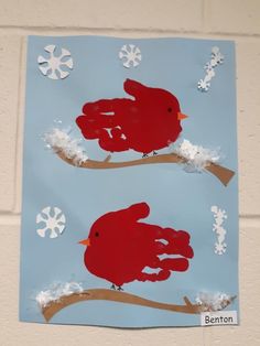 two red birds sitting on top of a branch with snow flakes in the background