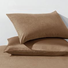 two pillows on top of each other in front of a white wall and brown sheets