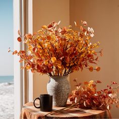 a vase filled with orange flowers next to a cup on a table near the ocean