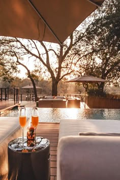 two glasses of wine sitting on top of a wooden table next to a swimming pool