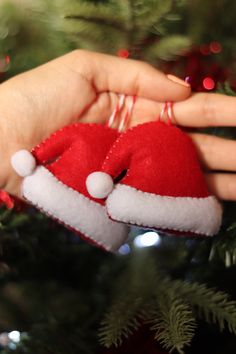 a hand holding a red and white santa hat ornament in front of a christmas tree