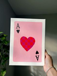 a hand holding up a pink playing card with hearts and spades on the back