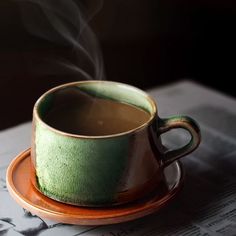 a green cup with steam rising out of it sitting on top of a saucer