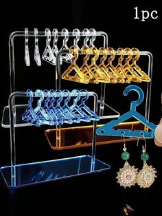 a person holding up a pair of earrings in front of a rack with hangers