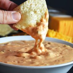 a hand dipping a tortilla chip into a bowl of quesadilla dip