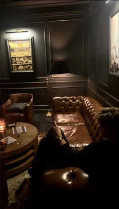 a dimly lit room with leather couches and tables in front of the wall, along with pictures on the walls