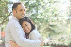 a man and woman embracing each other in front of trees with sunlight coming through the leaves