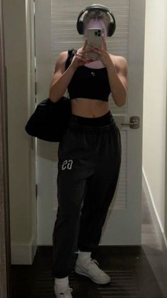 a woman taking a selfie in front of a mirror wearing headphones and black sweatpants