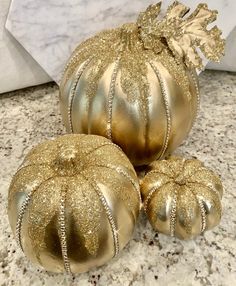 three gold pumpkins sitting on top of a marble counter