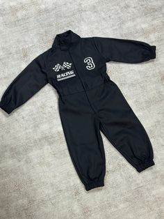 a baby's black snowsuit with white writing on the chest and feet, sitting on a gray surface