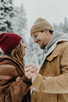 a man and woman are holding hands in the snow outside on a snowy day with trees in the background