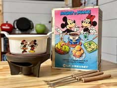 an old mickey mouse and minnie mouse cereal bowl with two spoons next to it