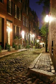 a cobblestone street at night in an old time town, with lights on