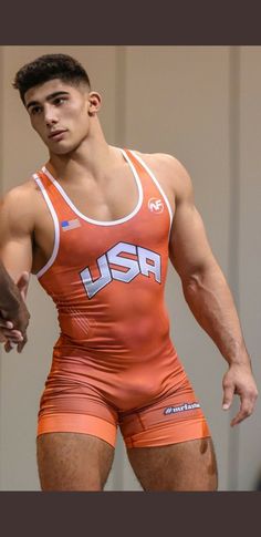 a man in an orange wrestling suit holding his hand out to the side while standing