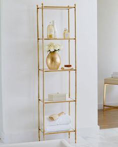 a gold shelf with white towels and flowers on it in the corner of a room