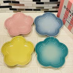 four different colored plates sitting on top of a white tiled counter next to a box