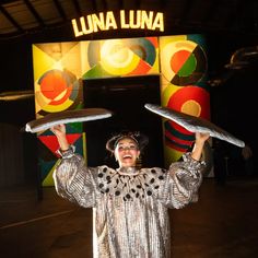 a woman is holding two plates in front of her head while standing under a sign that says lunaa lunaa