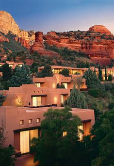 an adobe style building surrounded by trees in front of mountains with lights on at night