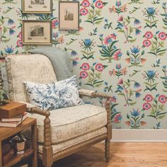 a living room with floral wallpaper and a chair in front of a table, framed pictures on the wall