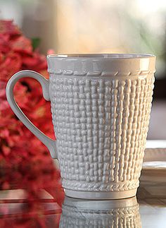 a white coffee cup sitting on top of a table next to a vase with red flowers