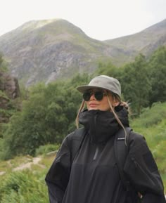 a woman wearing sunglasses and a hat standing in front of mountains