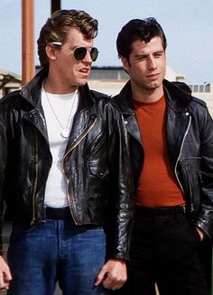 two men standing next to each other wearing black leather jackets and orange sweaters,