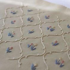 an embroidered cloth with flowers on it is laying on a tablecloth that has been stitched together