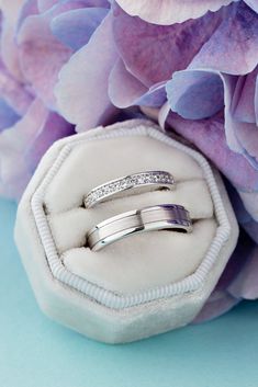 two wedding rings sitting on top of a white ring box next to purple and pink flowers