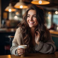 a woman sitting at a table with a cup of coffee in her hand and smiling