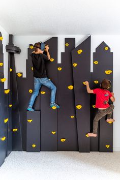 two boys climbing on the wall with yellow smiley faces painted on them and one boy holding a camera