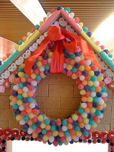 a gingerbread house made out of candy balls and other candies with a red bow on the front door