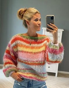 a woman taking a selfie in front of a mirror wearing a colorful sweater and jeans