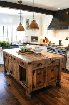 a large kitchen island in the middle of a wood floored area with two pendant lights hanging over it