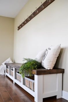 a bench with some plants on it and two white baskets under the seat, next to a wall