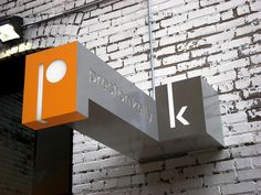 an orange and gray sign hanging from the side of a brick wall next to a light