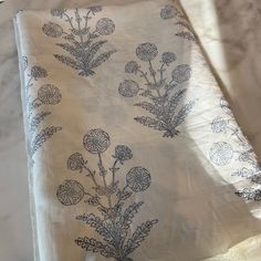 a white table cloth with blue flowers and leaves on it, sitting on a bed