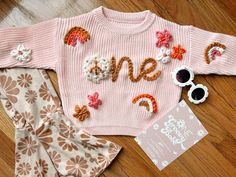 a pink sweater with the word one written on it next to two pairs of sunglasses