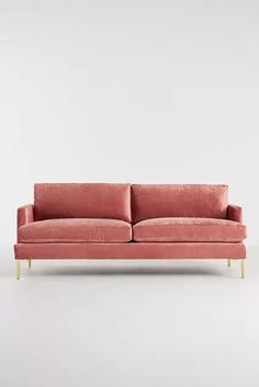 a pink velvet couch with gold legs on a white floor, in front of a wall