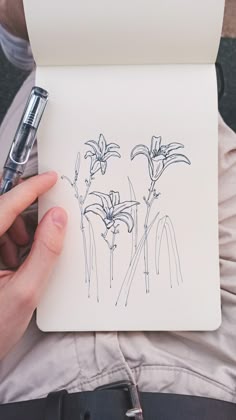 a person holding a pen and paper with flowers drawn on it in front of them