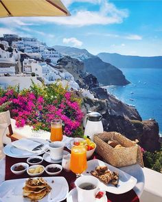 breakfast is served on the table overlooking the ocean and town below it with pink flowers in bloom