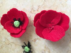 two red felt flowers with ladybugs in the center on a marble surface next to each other