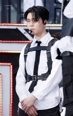 a man with black hair and suspenders is standing in front of a stage wearing a white shirt and black tie