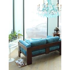 a blue couch sitting in front of a window next to a table with a glass chandelier hanging from it